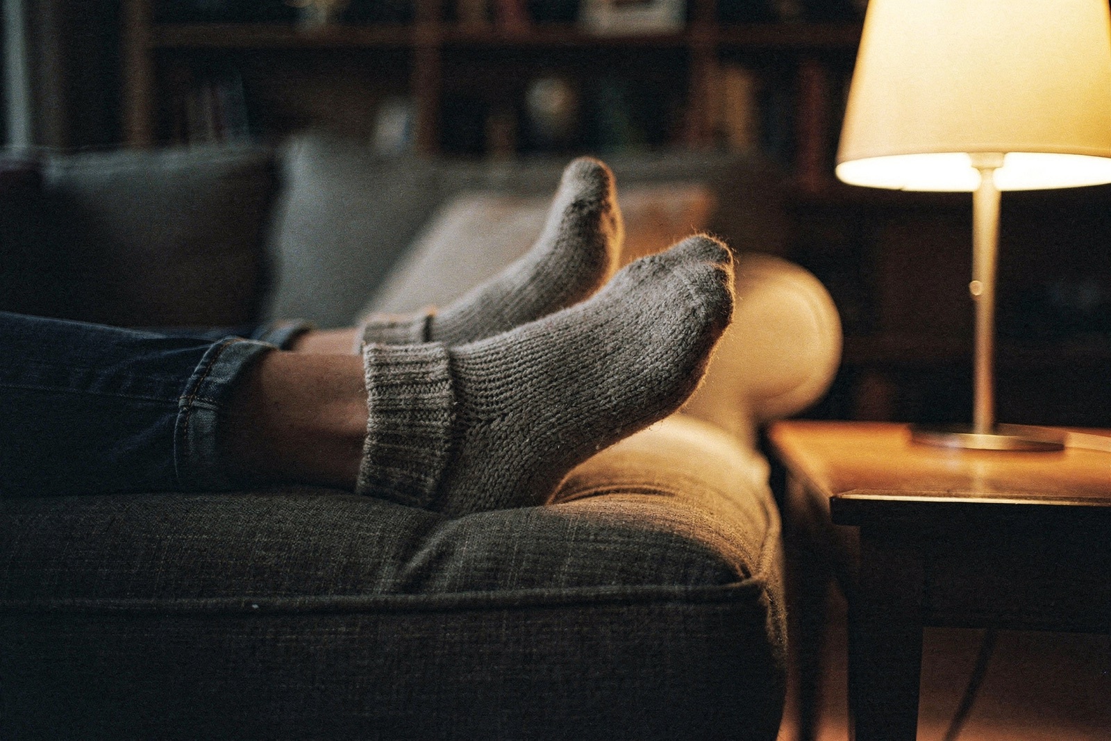 A pair of feet in soft wool socks propped on a cushion beside a lamp in the evening.
